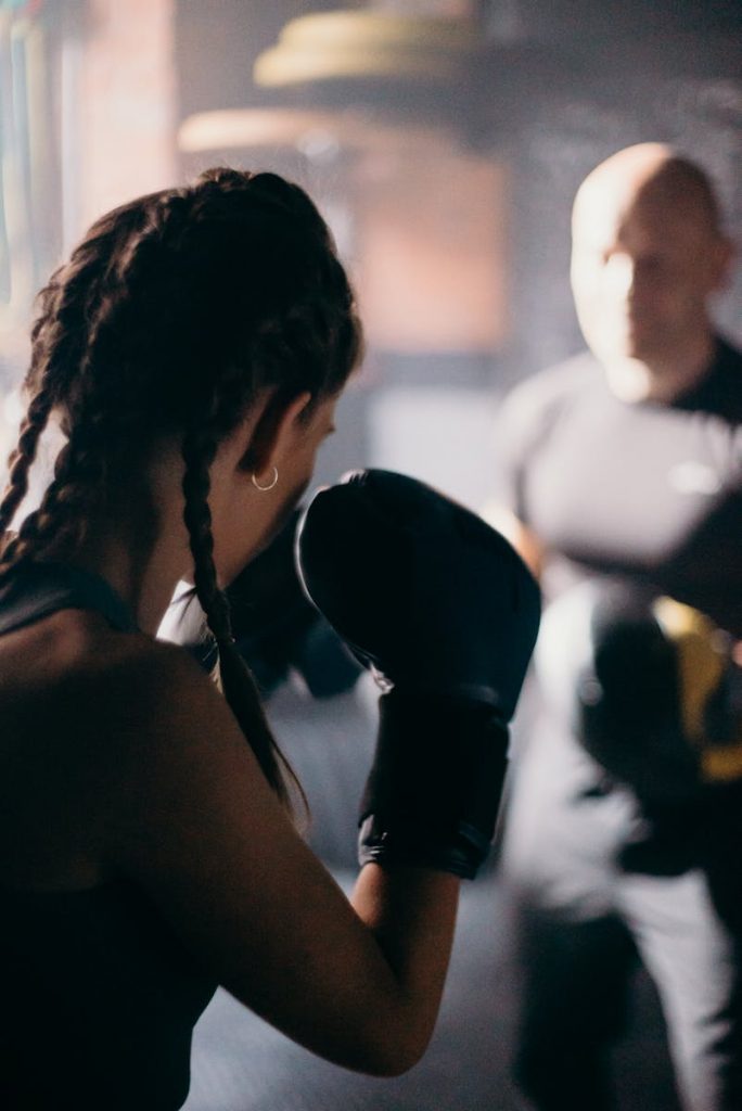 Female boxer practicing punches with a coach in a dim-lit gym.